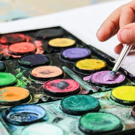 Young child holding a paint brush selecting a colour from a paint colour palet.