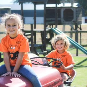 Two young girls on a tractor in an outdoor area, smiling and enjoying their time in a natural setting.
